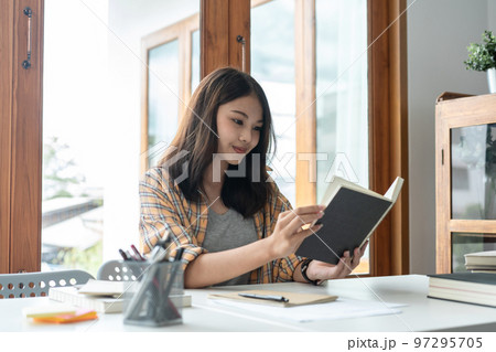 Young woman student reading textbook and doing homework assignment after using laptop to learning 97295705