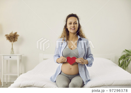 Happy pregnant woman holding red heart near her belly as sign of love for her unborn child. Happy pregnant woman holding red heart near her belly as sign of love for her unborn child. 97296378