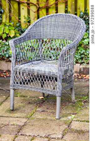 Rattan armchair in a garden patio or terrace on a sunny day in autumn. Rustic outdoor furniture in a calm and peaceful environment surrounded by nature. Cosy spot to enjoy a break with fresh air 97299088