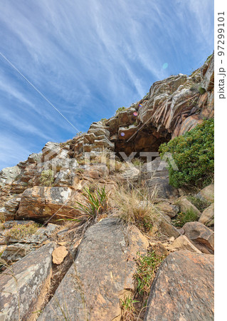Cliff at the side of mountain or island with cave to rest in after rock climbing, surrounded by plants, trees and nature in summer or spring. Closeup view from the bottom of a canyon with a blue sky 97299101