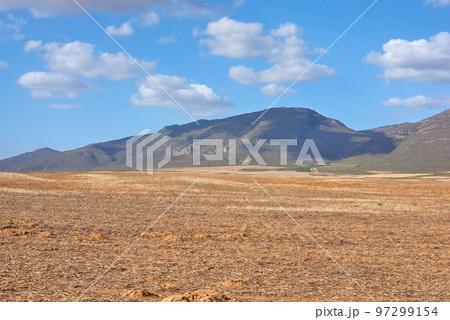 Farmland in the Western Cape of South Africa in the middle of the day. A mountain in a bare land with a cloudy blue sky. An empty farm with a nature view and a copy space. Farmland in the Western Cape of South Africa in the middle of the day. A mountain in a bare land with a cloudy blue sky. An empty farm with a nature view and a copy space. 97299154