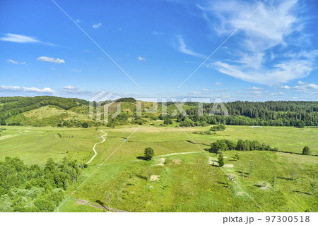 Landscape of a countryside with a cloudy blue sky and copyspace. Wide drone view of green forestry and cultivated grassland. Beautiful landscape of flat land surrounded by forest trees with copyspace 97300518