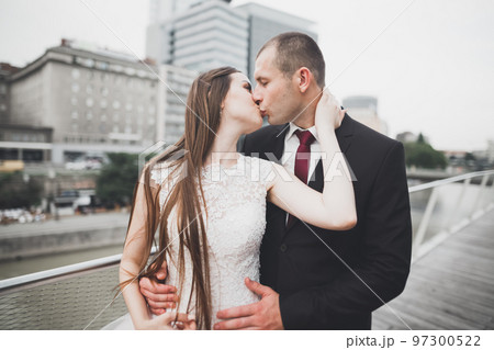 Beautiful bride and groom embracing and kissing on their wedding day outdoors Beautiful bride and groom embracing and kissing on their wedding day outdoors 97300522