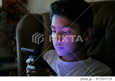 teenage boy sitting on sofa using smart phone at night teenage boy sitting on sofa using smart phone at night 97304729