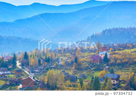 Aerial view of an autumn small village in a valley and mountains in a blue haze 97304732