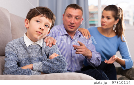 Frowning boy with mother and father berating him Frowning boy with mother and father berating him 97310114