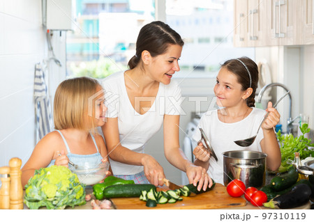 Young woman and two daughters cooking together Young woman and two daughters cooking together 97310119