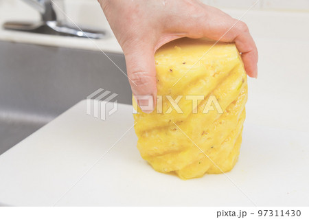 【皮削ぎの終わったパイナップルを切っていく】 97311430