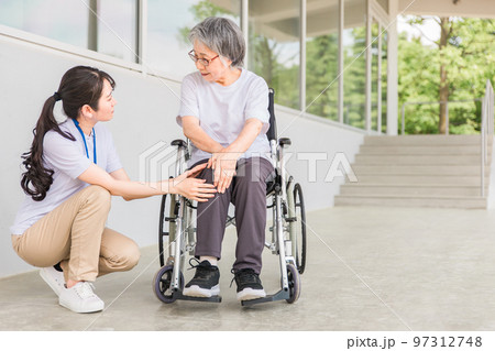 老人ホームで車椅子に乗りながらリハビリする高齢者と介護士（膝・膝痛） 97312748
