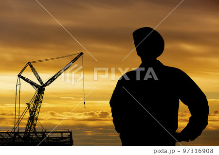 夕日を背景に建設現場でそびえるクレーンと作業員のシルエット 夕日を背景に建設現場でそびえるクレーンと作業員のシルエット 97316908