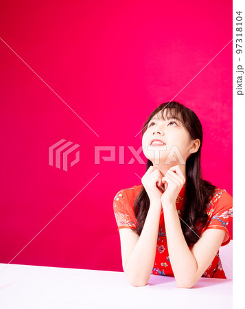 伝統的なチャイナドレスを着てあごに手をあて、赤い背景に横を見る美しいアジア人女性。 97318104