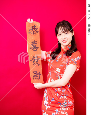 伝統的なチャイナドレスを着たアジアの若い女性は、赤い背景に新年を意味する言葉で新年を祝うために、中国 97318138