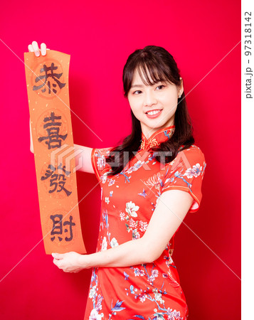 伝統的なチャイナドレスを着たアジアの若い女性は、赤い背景に新年を意味する言葉で新年を祝うために、中国 97318142