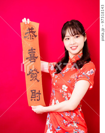 伝統的なチャイナドレスを着たアジアの若い女性は、赤い背景に新年を意味する言葉で新年を祝うために、中国 97318143