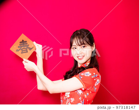 伝統的なチャイナドレスを着たアジアの若い女性は、赤い背景に新年を意味する言葉で新年を祝うために、中国 97318147