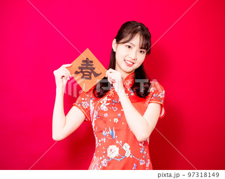 伝統的なチャイナドレスを着たアジアの若い女性は、赤い背景に新年を意味する言葉で新年を祝うために、中国 97318149