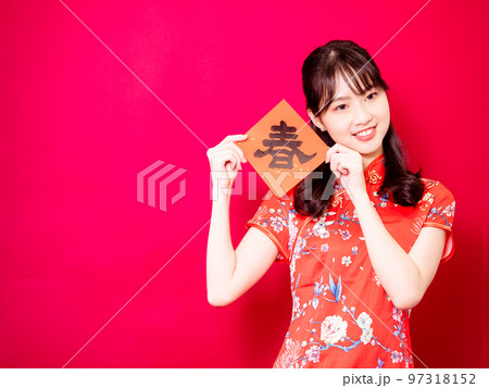 伝統的なチャイナドレスを着たアジアの若い女性は、赤い背景に新年を意味する言葉で新年を祝うために、中国 97318152