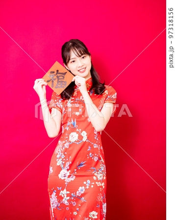 伝統的なチャイナドレスを着たアジアの若い女性は、赤い背景に新年を意味する言葉で新年を祝うために、中国 97318156