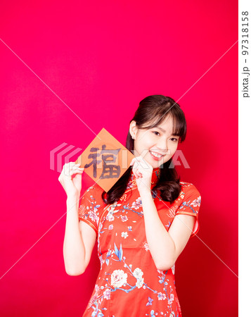 伝統的なチャイナドレスを着たアジアの若い女性は、赤い背景に新年を意味する言葉で新年を祝うために、中国 97318158