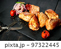 Close-up appetizing pork shish kebab on a black stone cutting board. Red onion, cherry tomatoes and two forks. Soft focus. Copy space 97322445