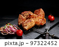 Appetizing pork shish kebab on a black stone cutting board. Red onion, cherry tomatoes and two forks. Soft focus 97322452