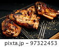 Close-up appetizing BBQ chicken thighs on a black cutting board. Soft focus. 97322453
