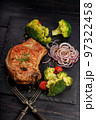Appetizing BBQ pork loin with vegetables on a black stone board. Roast pork and broccoli. Vertical shot. Copy space. Old rustic wooden background 97322458