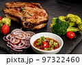 Close-up BBQ pork loin with spicy sauce and vegetables on a black stone board. Selective focus. Old rustic wooden background 97322460