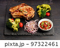 Delicious BBQ Pork Loin with spicy sauce and vegetables on a black stone board. Top view. Old rustic wooden background 97322461