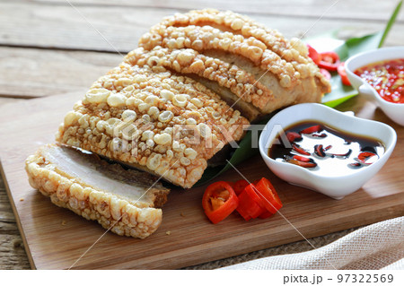 Closeup crispy pork belly or deep fried pork on wooden board with black soy sauce with red chili and spicy seafood sauce in background. 97322569