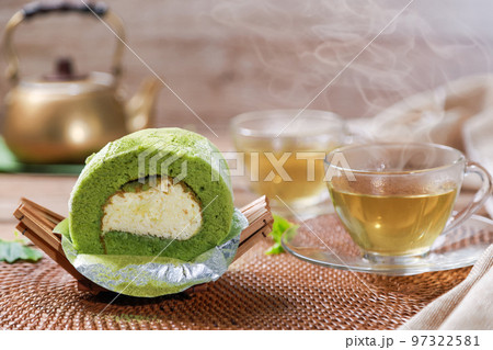 Matcha Green Tea Roll Cake with white cream inside and hot green tea in the cup background. Foods or dessert concept. 97322581