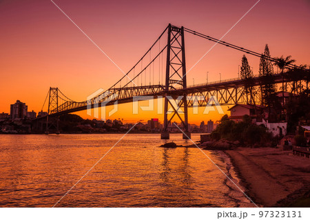 Hercilio luz cable bridge with sunset and reflection on water in Florianopolis Hercilio luz cable bridge with sunset and reflection on water in Florianopolis 97323131