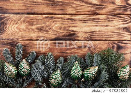 Green branches of a Christmas tree with decorations in the form of green cones on a wooden background with a place for text. Top view 97325302
