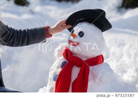 Caucasian woman sculpts a snowman from the snow. The carrot is the place of the nose. 97325587