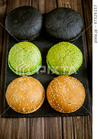 Top down view of variety of six hamburger buns on wooden table. Black, green, yellow buns Top down view of variety of six hamburger buns on wooden table. Black, green, yellow buns 97326157