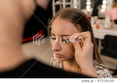 Makeup artist paints eyelashes to a woman in a beauty salon. 97329150