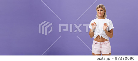 Ew take disgusting thing away from me. Stylish feminine good-looking blond woman in cropped top with tanned skin and pierced belly looking at creepy think with dislike and aversion over purple wall Ew take disgusting thing away from me. Stylish feminine good-looking blond woman in cropped top with tanned skin and pierced belly looking at creepy think with dislike and aversion over purple wall 97330090