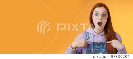 Shocked emotive surprised redhead european woman wearing glasses hoodie drop jaw gasping stunned pointing herself full disbelief cannot believe win being picked look impressed orange background 97330204