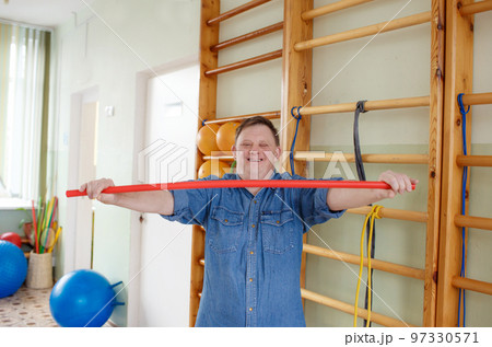 a young man with down syndrome is engaged in a gym with a gymnastic stick. rehabilitation process. 97330571