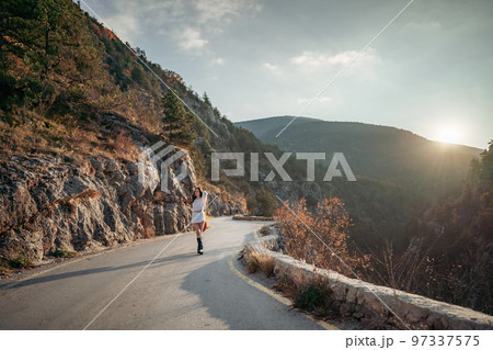 The woman is dear to the mountains. A woman in a white sweater, black boots and a hat walks along a winding alpine path between the mountains at the end of summer at sunset. Travel concept. The woman is dear to the mountains. A woman in a white sweater, black boots and a hat walks along a winding alpine path between the mountains at the end of summer at sunset. Travel concept. 97337575
