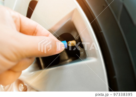 The driver is putting on the wheel tire valve cap of a car after inflating 97338395