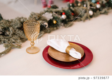Traditional Christmas table setting. Burgundy and gold plate, linen napkin, fir branches and glass goblet. Festive dinner decor 97339877