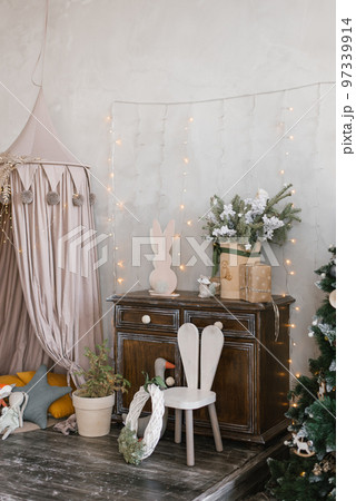 Interior of a children's room decorated for Christmas. Awning bed with toys and pillows, a tree, a wardrobe and an armchair in gray beige colors Interior of a children's room decorated for Christmas. Awning bed with toys and pillows, a tree, a wardrobe and an armchair in gray beige colors 97339914