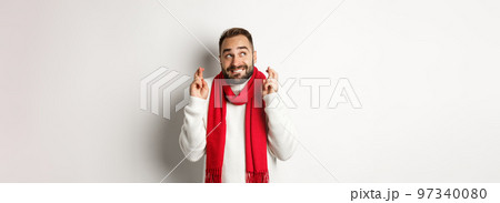 Christmas holidays and New Year concept. Hopeful man making wish with fingers crossed, waiting for gifts, standing over white background Christmas holidays and New Year concept. Hopeful man making wish with fingers crossed, waiting for gifts, standing over white background 97340080