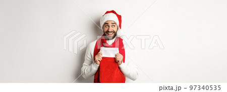 Winter holidays and shopping concept. Excited handsome man planning new year, holding Christmas sock for gifts and thinking, standing over white background Winter holidays and shopping concept. Excited handsome man planning new year, holding Christmas sock for gifts and thinking, standing over white background 97340535