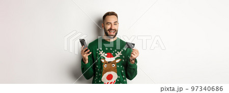 New Year, online shopping and christmas concept. Happy bearded man using mobile phone and credit card, winking at camera, order something in internet, white background New Year, online shopping and christmas concept. Happy bearded man using mobile phone and credit card, winking at camera, order something in internet, white background 97340686
