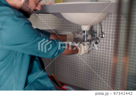 Close up of plumber is repairing faucet of a sink at bathroom. Good quality plumbing company service Close up of plumber is repairing faucet of a sink at bathroom. Good quality plumbing company service 97341442