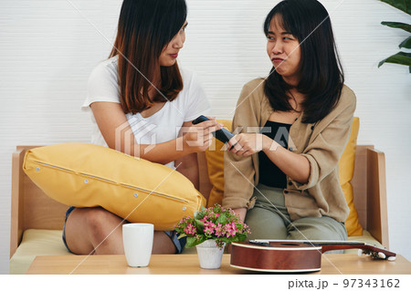 Playful young adult two sisters holding and snatching black remote control Playful young adult two sisters holding and snatching black remote control 97343162
