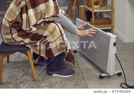 Man sitting at home in winter, feeling cold and warming up his hands by an electric heater Man sitting at home in winter, feeling cold and warming up his hands by an electric heater 97346890
