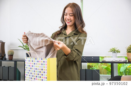 Excited smile female shopper holding ordered shirt, Happy Asian young customer woman opening shopping bag package after ordered new fashion clothes at home, shopping online delivery shipping Excited smile female shopper holding ordered shirt, Happy Asian young customer woman opening shopping bag package after ordered new fashion clothes at home, shopping online delivery shipping 97350102
